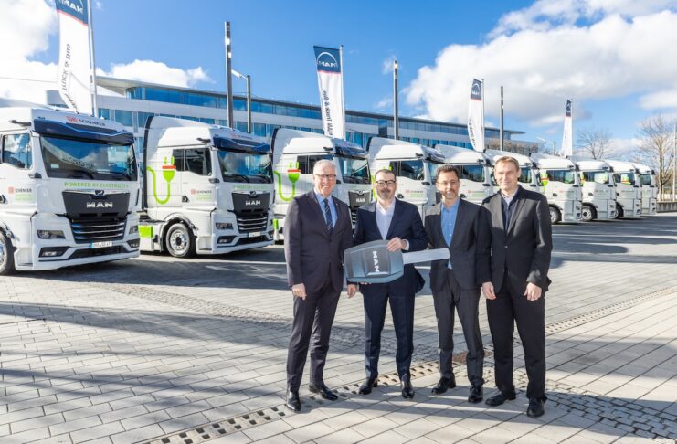 MAN eTGX MAN eTrucks im Hintergrund und im Vordergrund Vier Mitarbeiter von MAN und DB SCHENKER